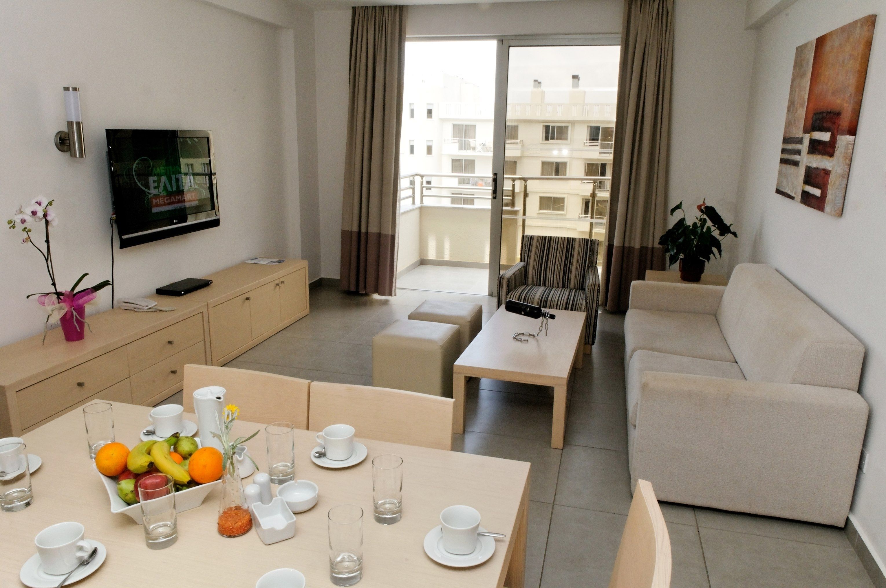 A modern living room with a dining area, a sofa, a TV mounted on the wall, and a balcony with curtains.