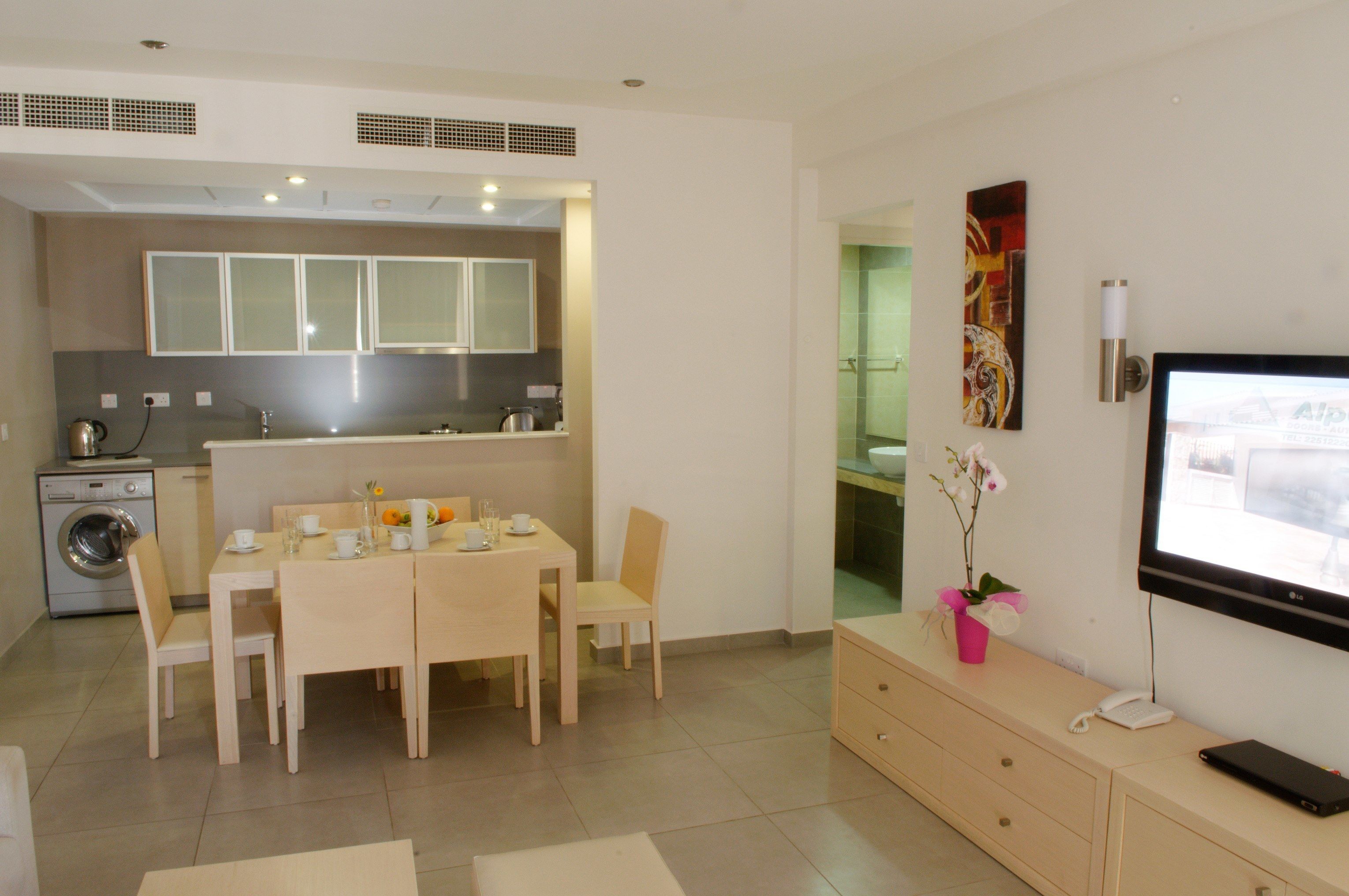 Una sala moderna con comedor, televisor y lavadora al fondo.