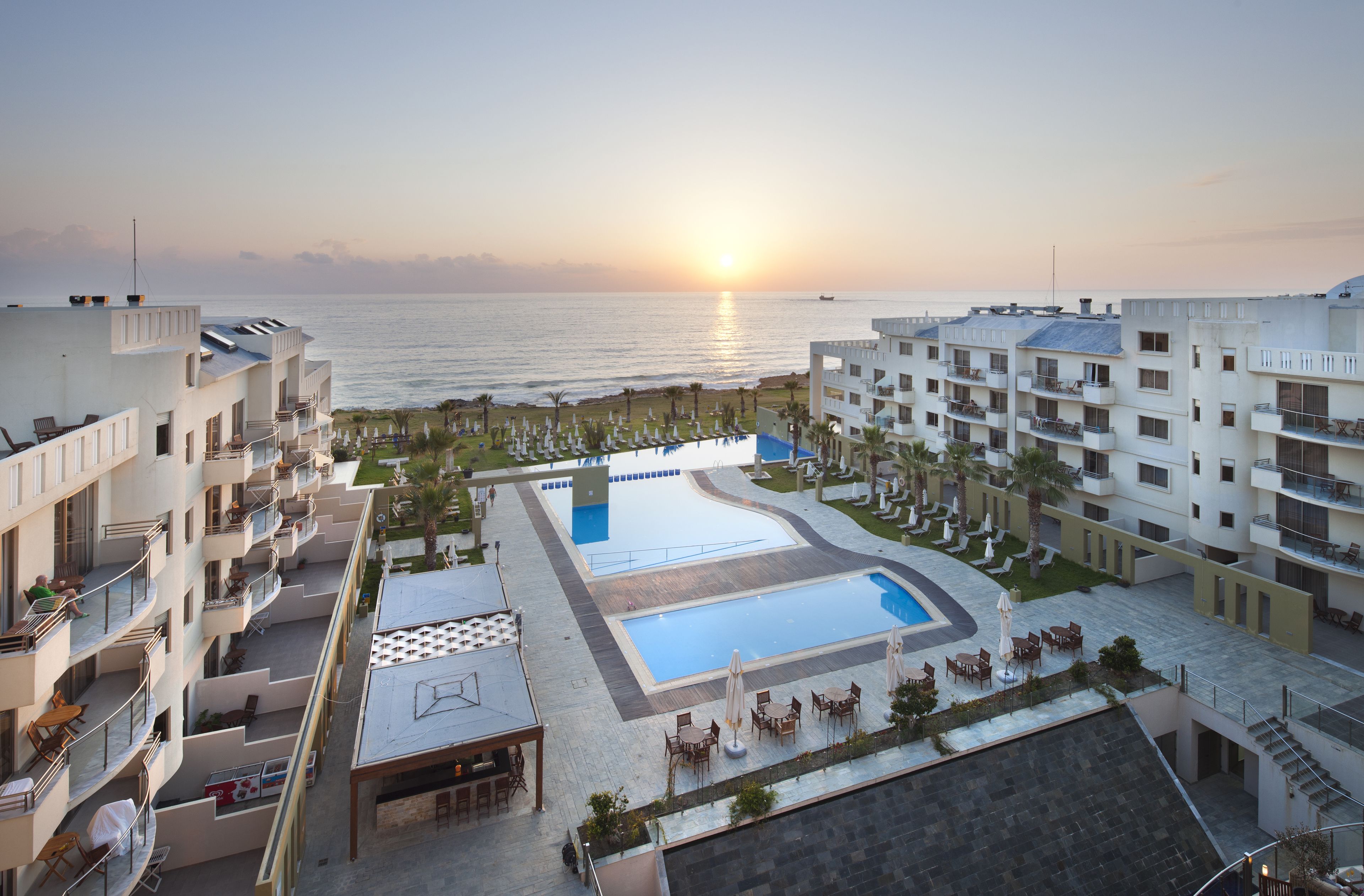 A hotel with a pool, outdoor seating, and a view of the sea at sunset.