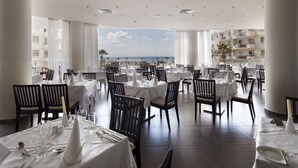 Un restaurante con mesas dispuestas para comer, amplias ventanas que ofrecen vistas al mar y una decoración interior moderna.