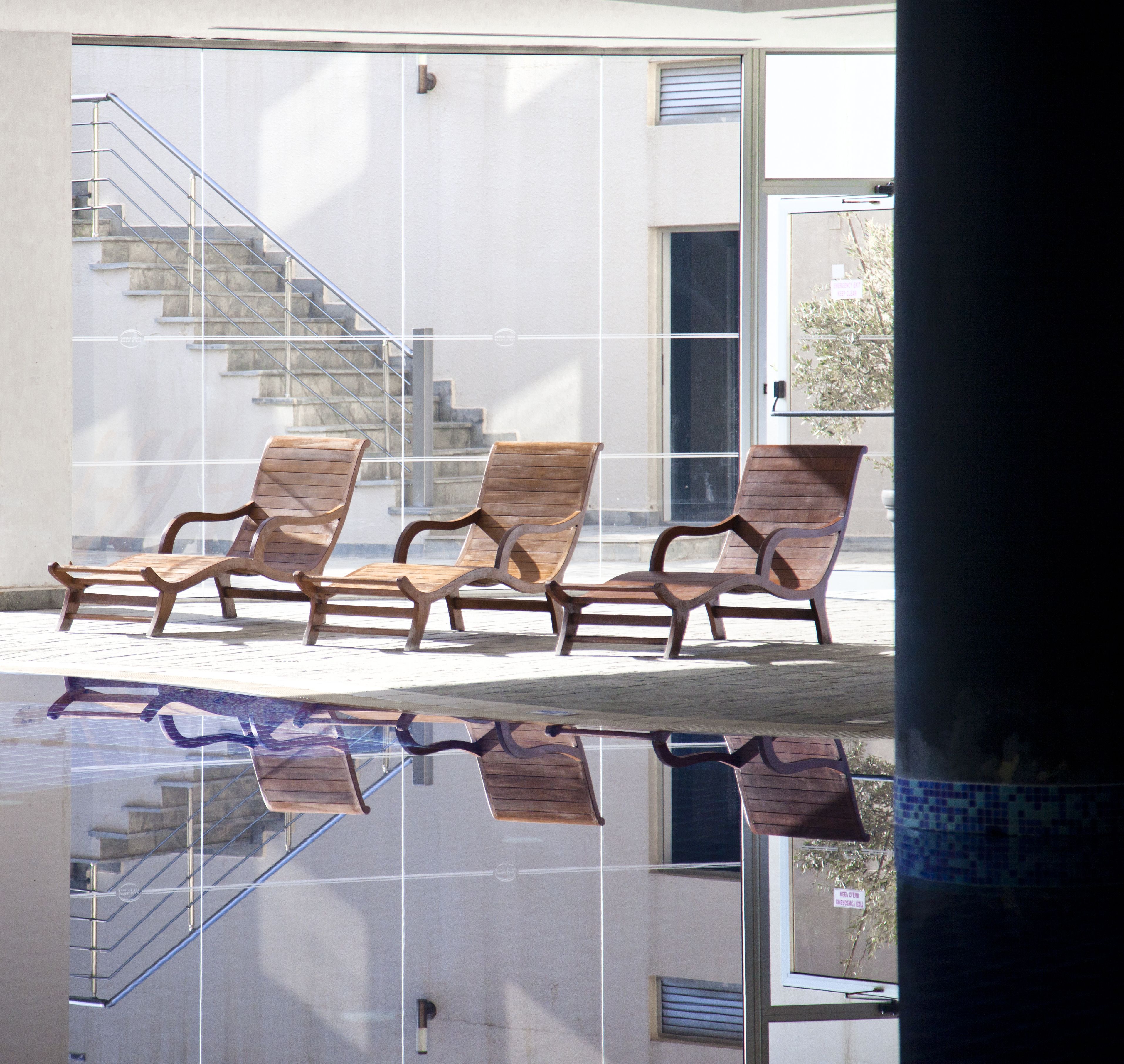 A pool area with wooden lounge chairs and a glass floor.