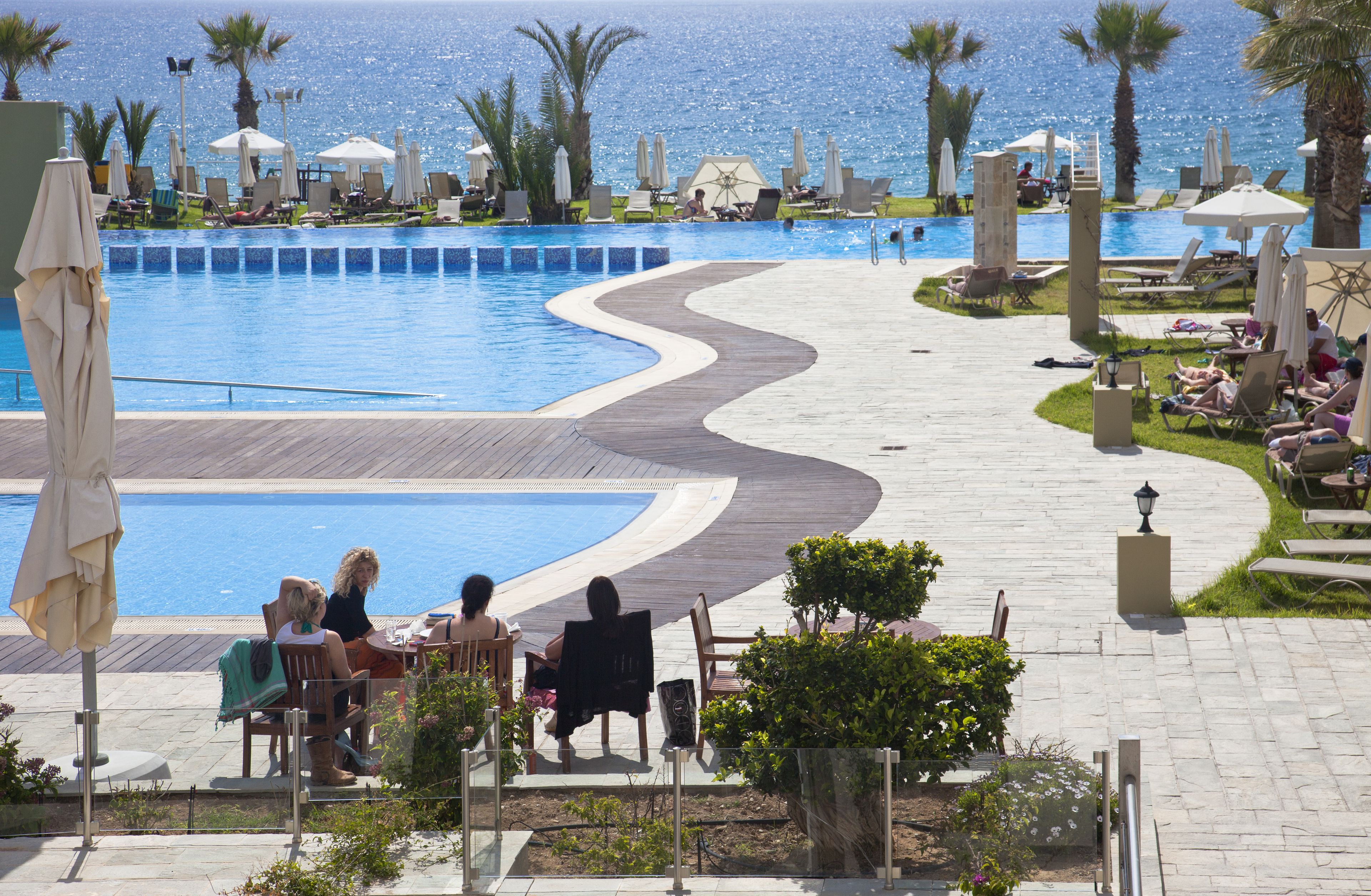 Un espace aménagé au bord de la piscine, avec des chaises longues et des parasols, une terrasse en bois et une vue sur la mer.