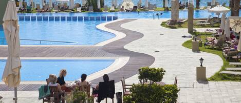 A poolside area with lounge chairs and umbrellas, a wooden deck, and a view of the sea.