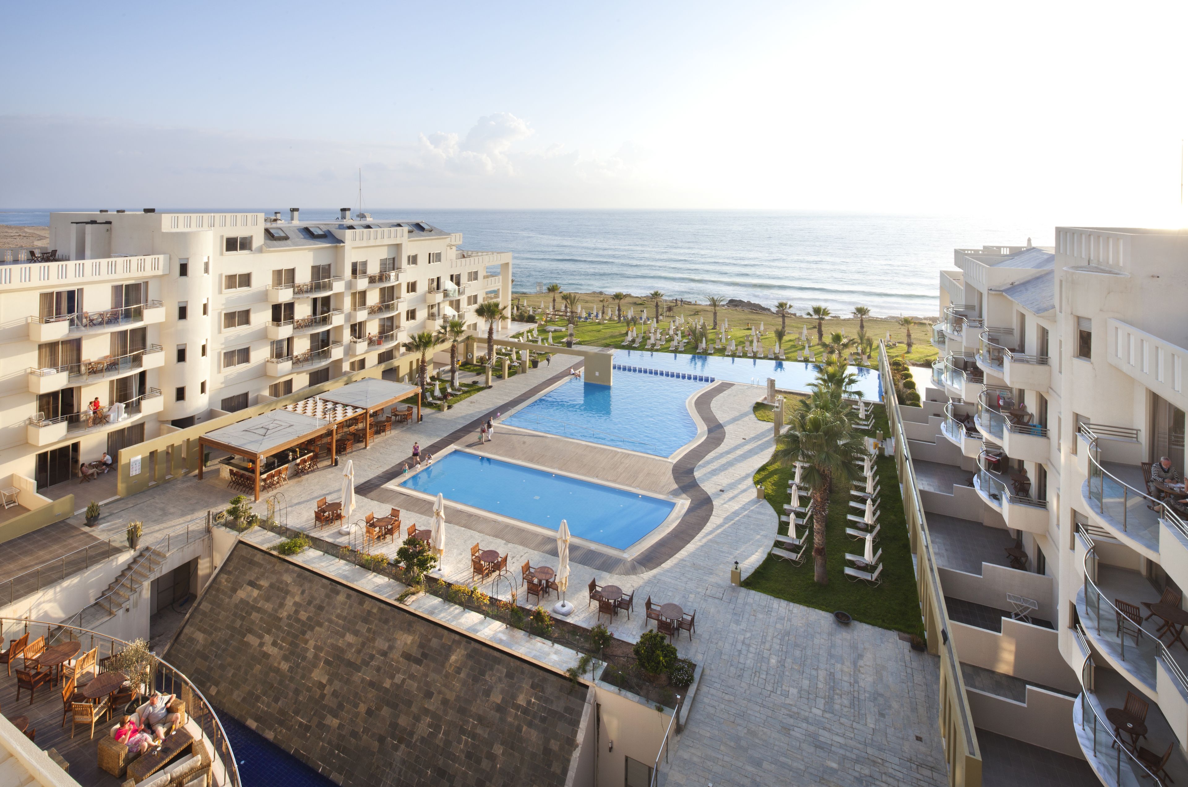 Un hotel con varios pisos, una piscina central y vistas al océano.