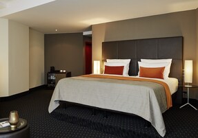 Ein Hotelzimmer mit einem großen Bett, einem Nachttisch mit Lampe, einer kleinen Kommode und einem runden Tisch mit einer Dekoration.