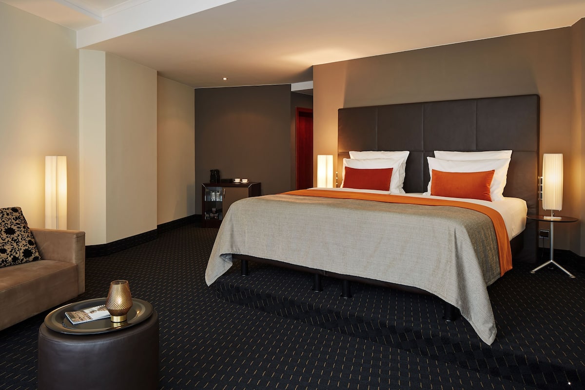 Una habitación de hotel con una cama grande, un sofá, una mesita auxiliar y una lámpara.
