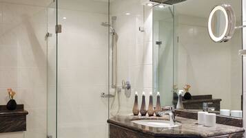 A modern bathroom with a glass-enclosed shower, a marble sink, and a large mirror with a ring light.