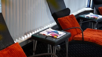 A room with black and orange chairs, a glass table with a magazine, and a window with blinds.