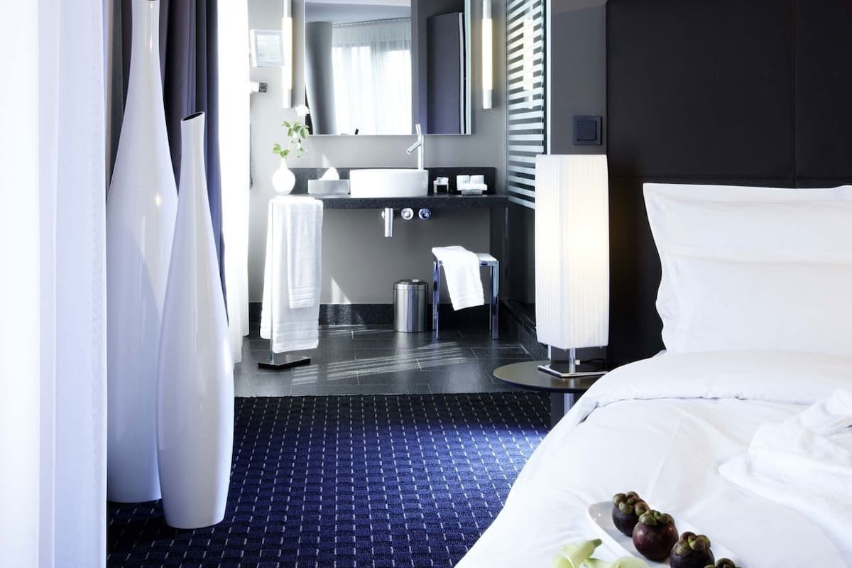 Habitación de hotel con cama, baño con lavamanos y espejo.