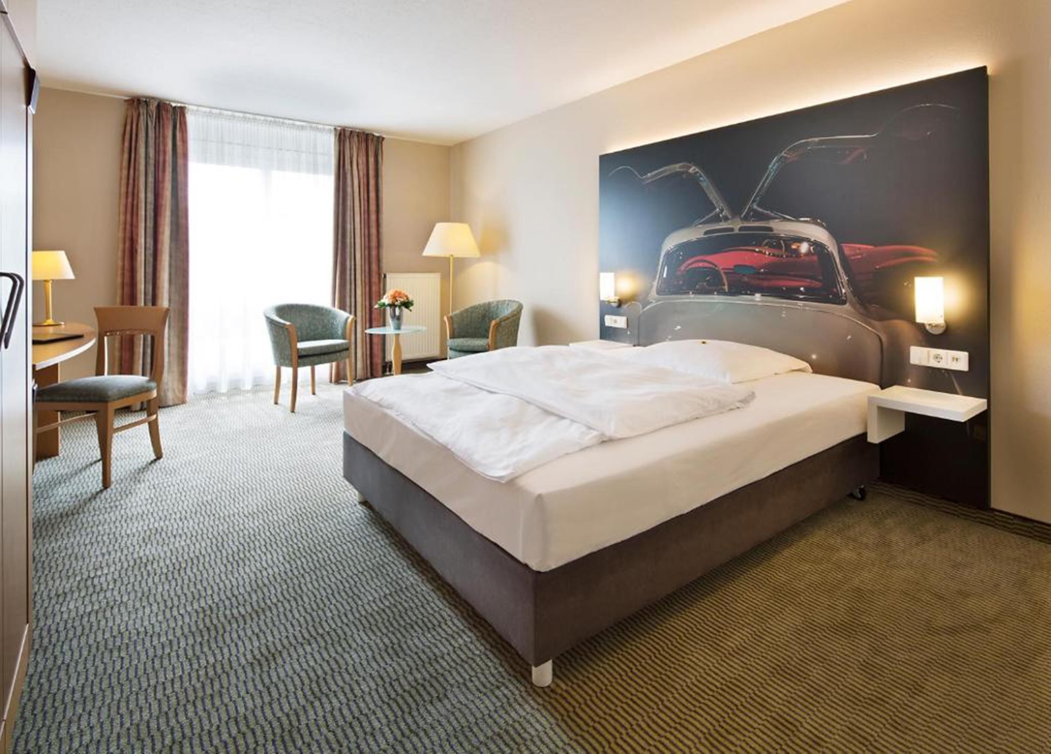 A hotel room with a large bed, two chairs, a desk, and a wall-mounted TV.