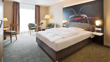 A hotel room with a large bed, two chairs, a desk, and a wall-mounted TV.