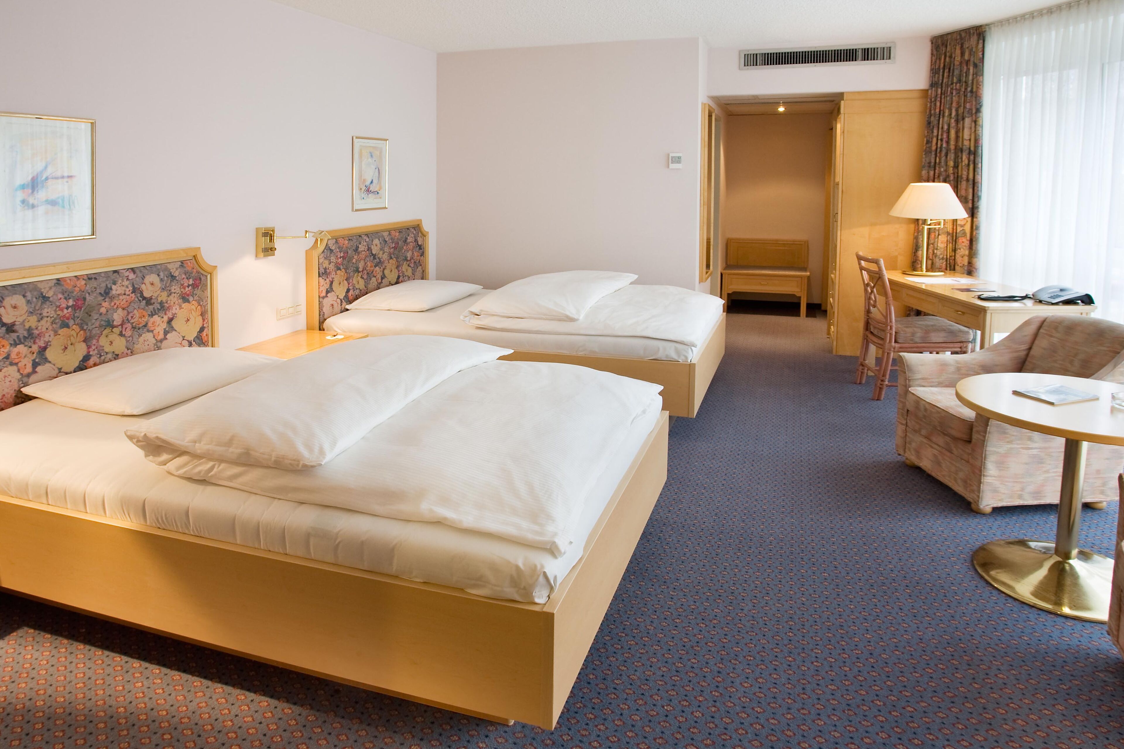Hotellihuone, jossa on kaksi sänkyä, työpöytä, tuoli ja pieni pöytä.