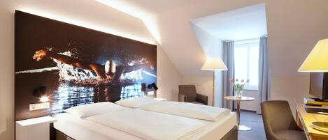 Una habitación de hotel con una cama grande, un escritorio, una silla, una lámpara y un cuadro en la pared.