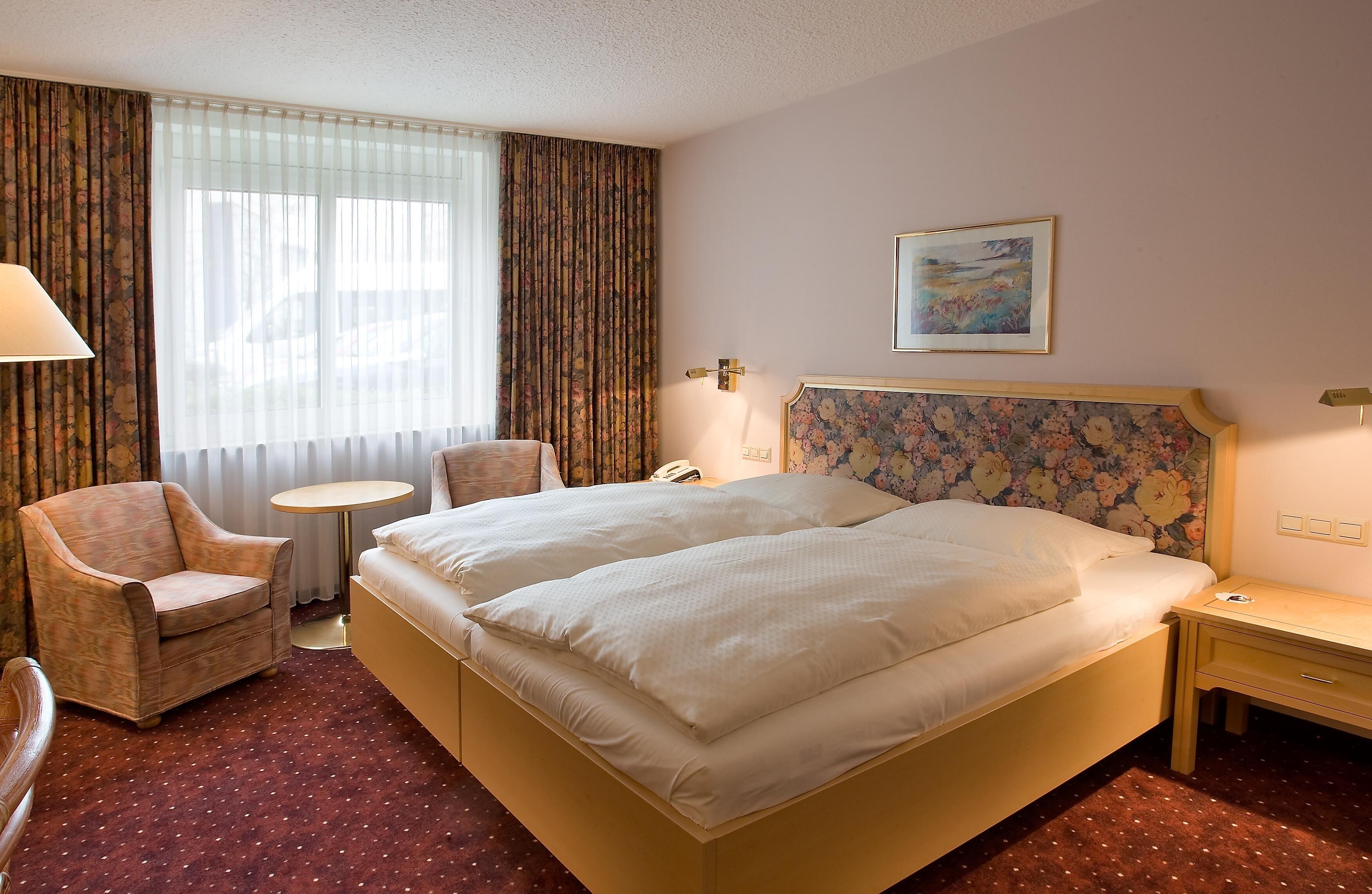 Una habitación de hotel con cama doble, una silla, una mesita redonda y una mesita de noche.
