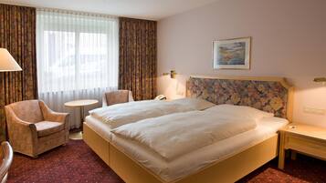 Una habitación de hotel con cama doble, una silla, una mesita redonda y una mesita de noche.