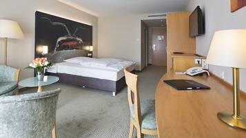 Una habitació d'hotel amb llit, escriptori, cadira, televisió i un quadre a la paret.