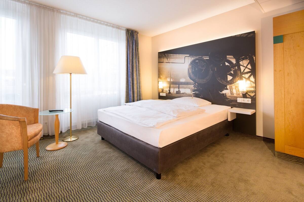A hotel room with a large bed, a desk, a chair, and a painting on the wall.