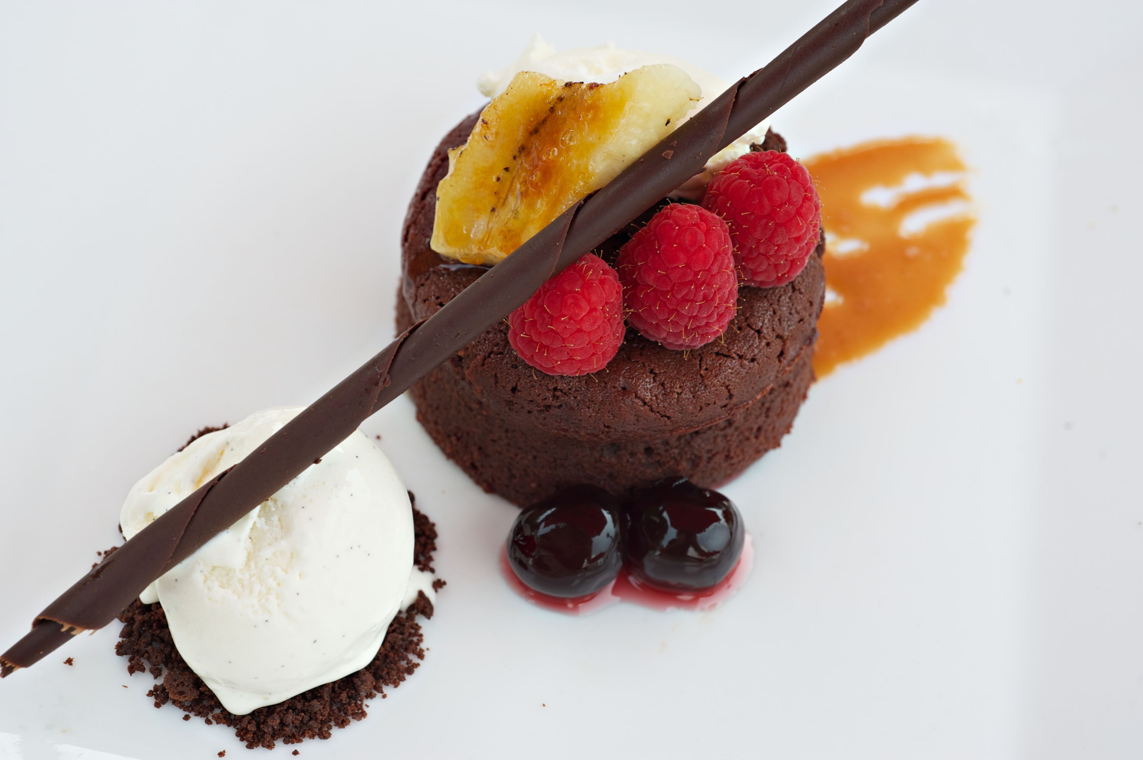 A dessert with chocolate cake, raspberries, cherries, and a banana slice.
