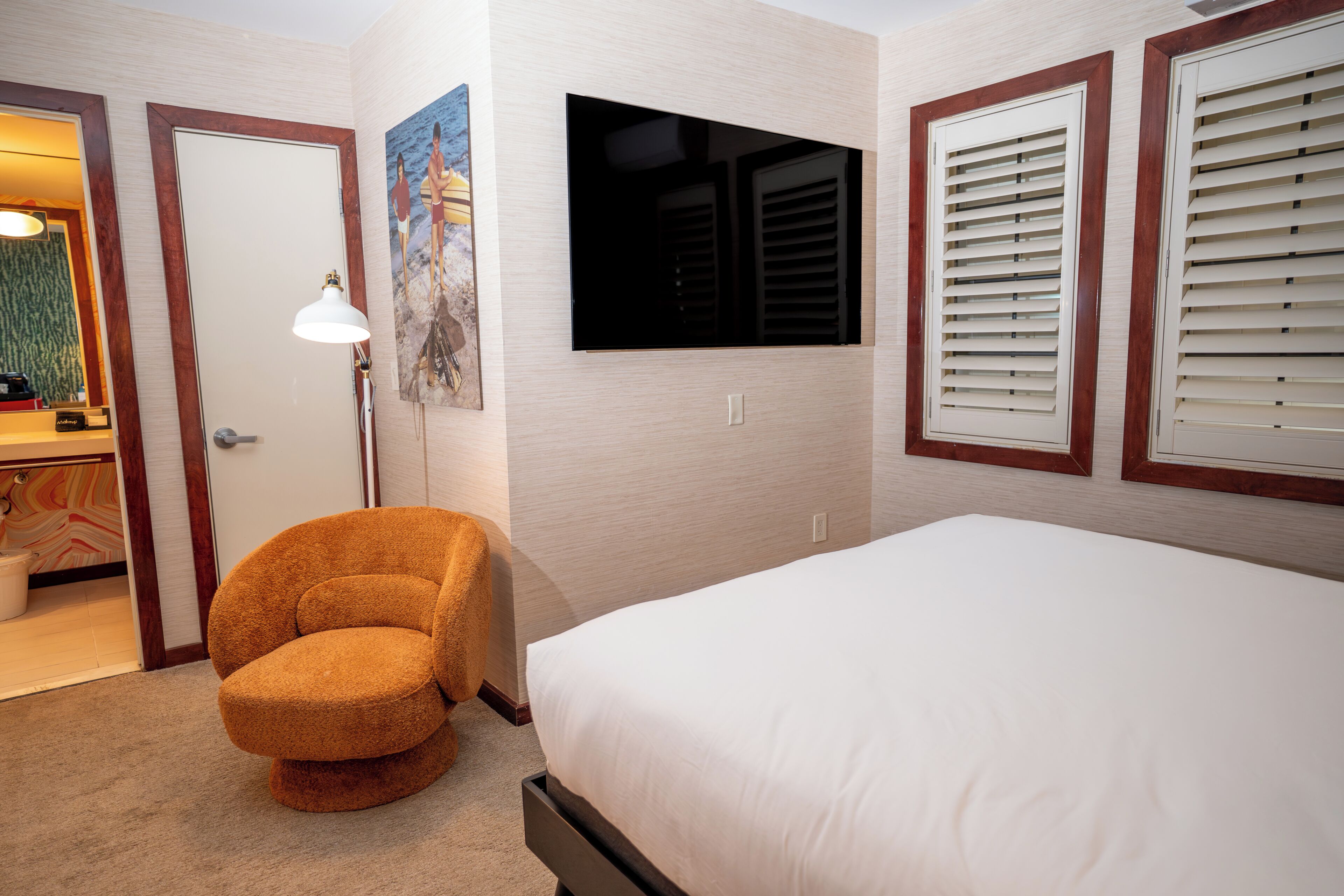 Une chambre d’hôtel avec un lit, une chaise, un téléviseur fixé au mur et une porte.