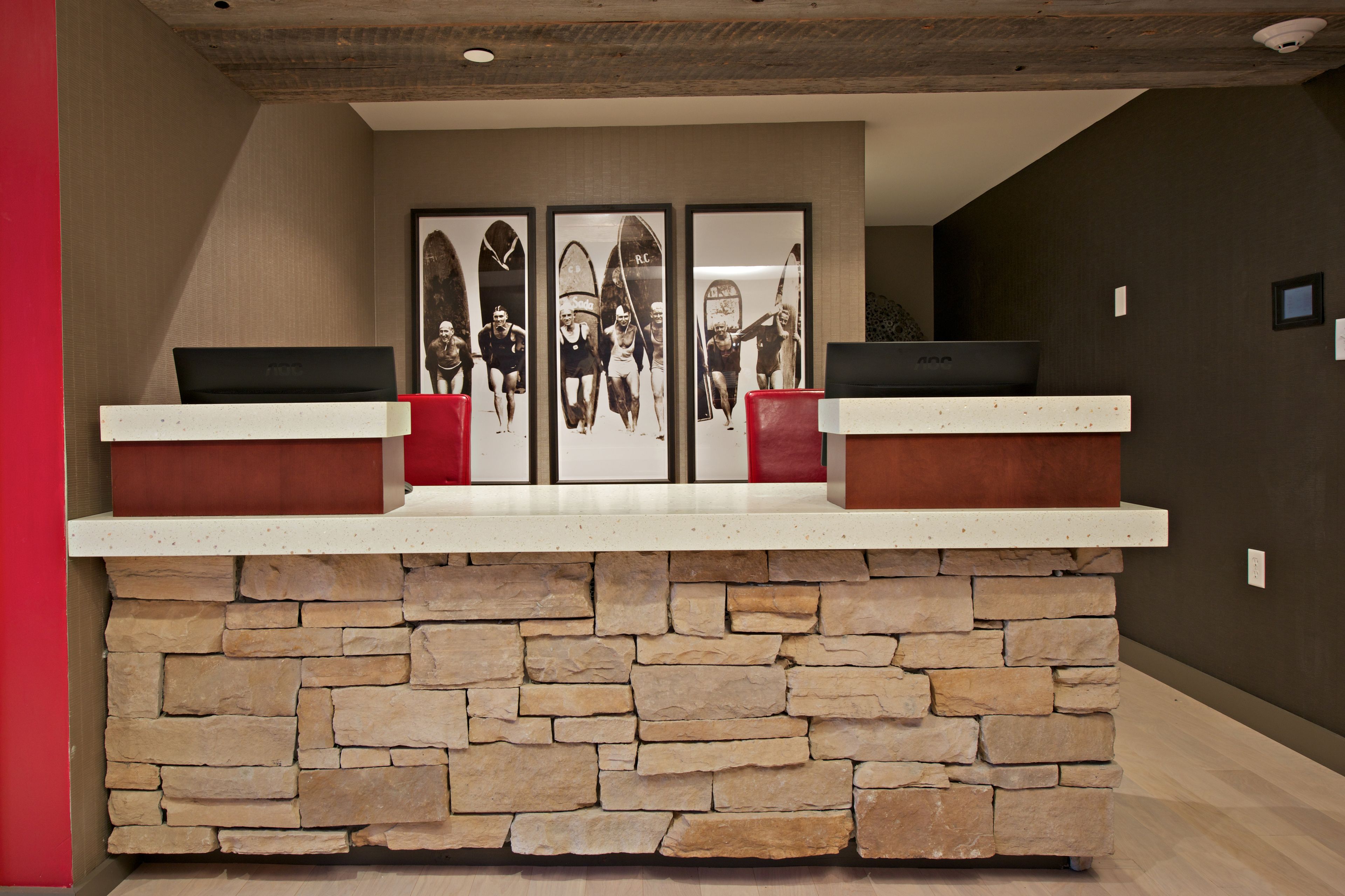 A reception desk with a stone base and two red cushioned chairs.