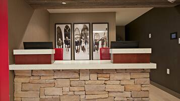 A reception desk with a stone base and two red cushioned chairs.