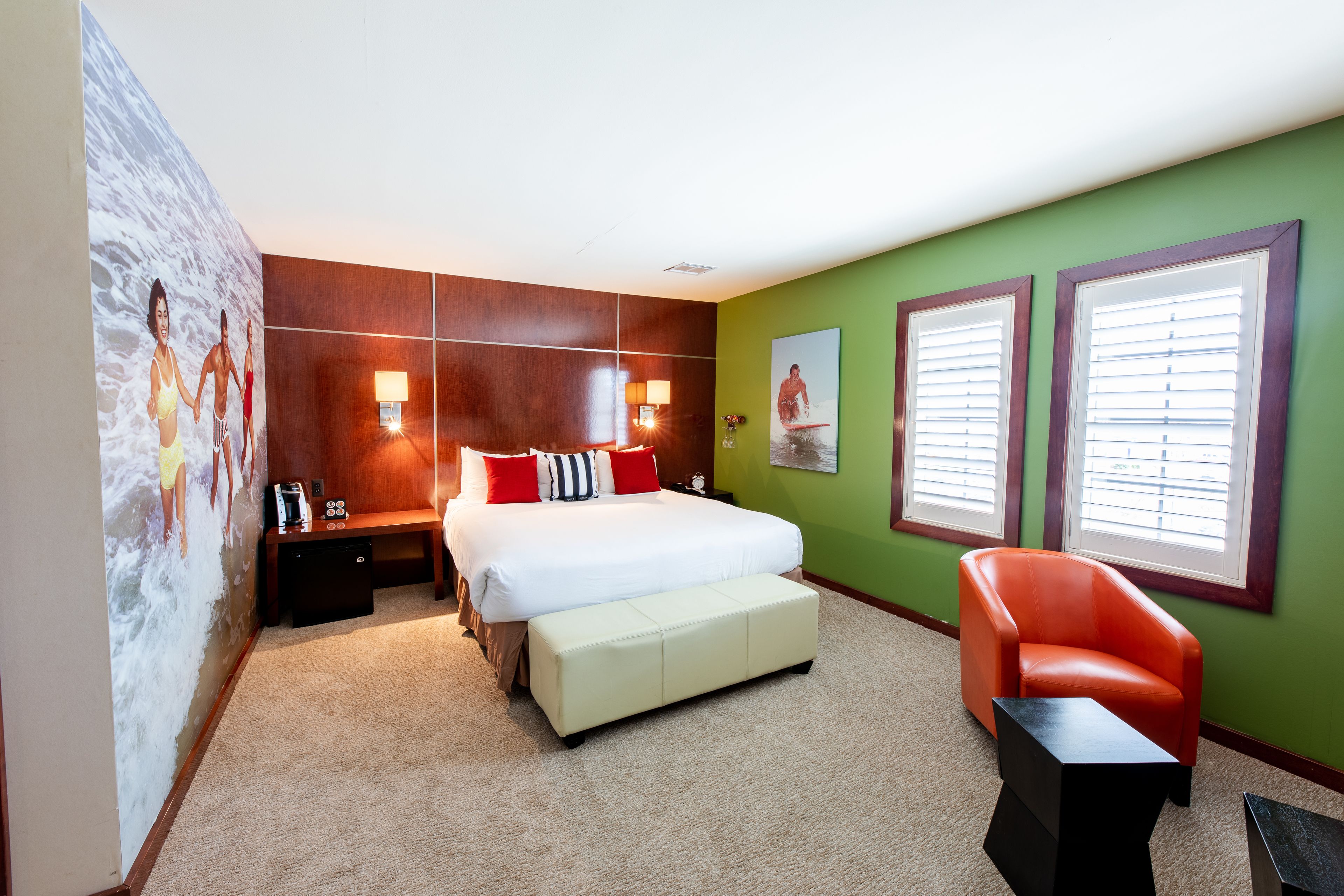 A hotel room with a bed, a bench, a chair, a nightstand, and a wall with a mural.