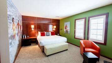 A hotel room with a bed, a bench, a chair, a nightstand, and a wall with a mural.