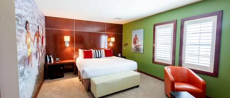 A hotel room with a bed, a bench, a chair, a nightstand, and a wall with a mural.