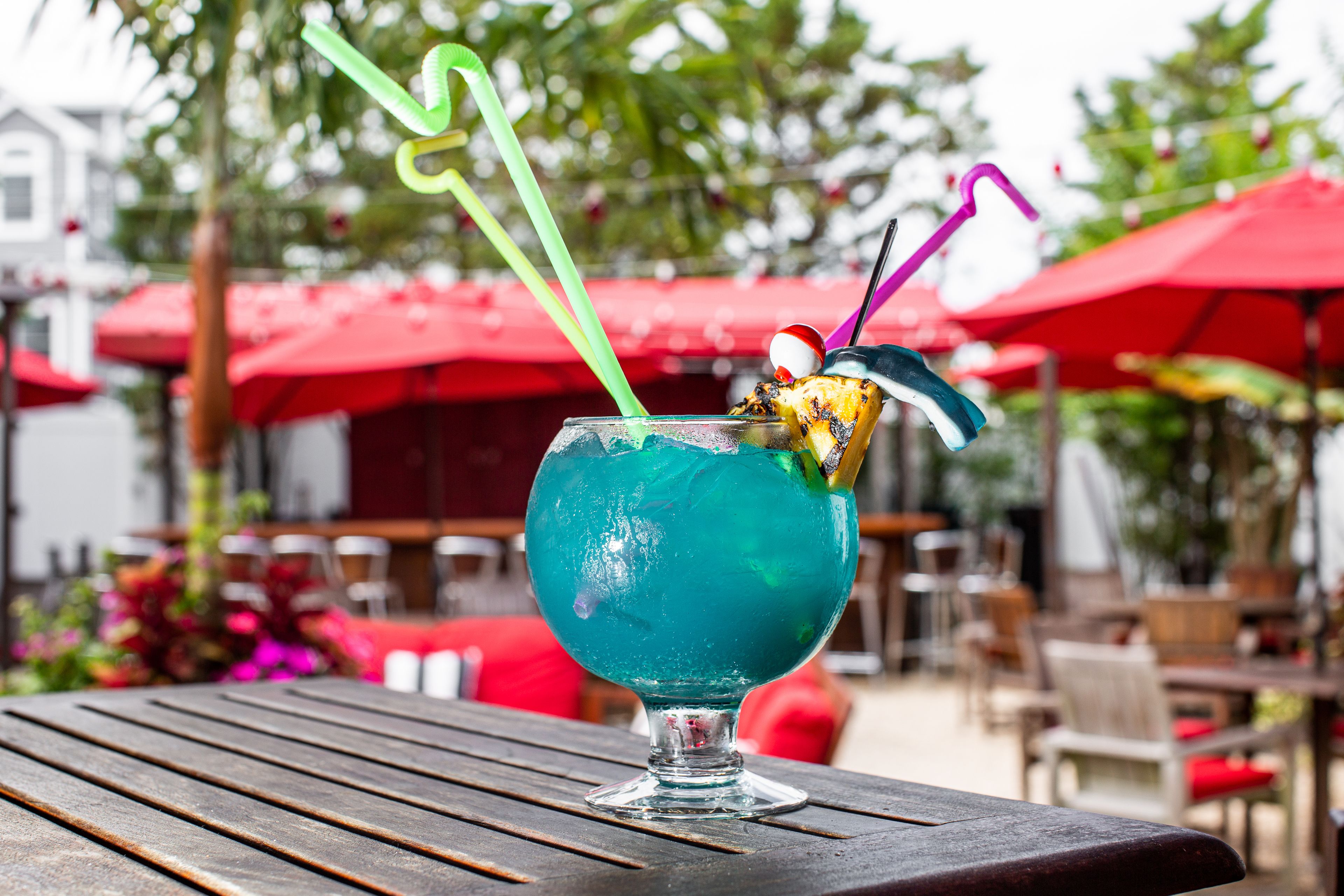 A tropical cocktail in a glass with a straw, set on a wooden table outdoors.