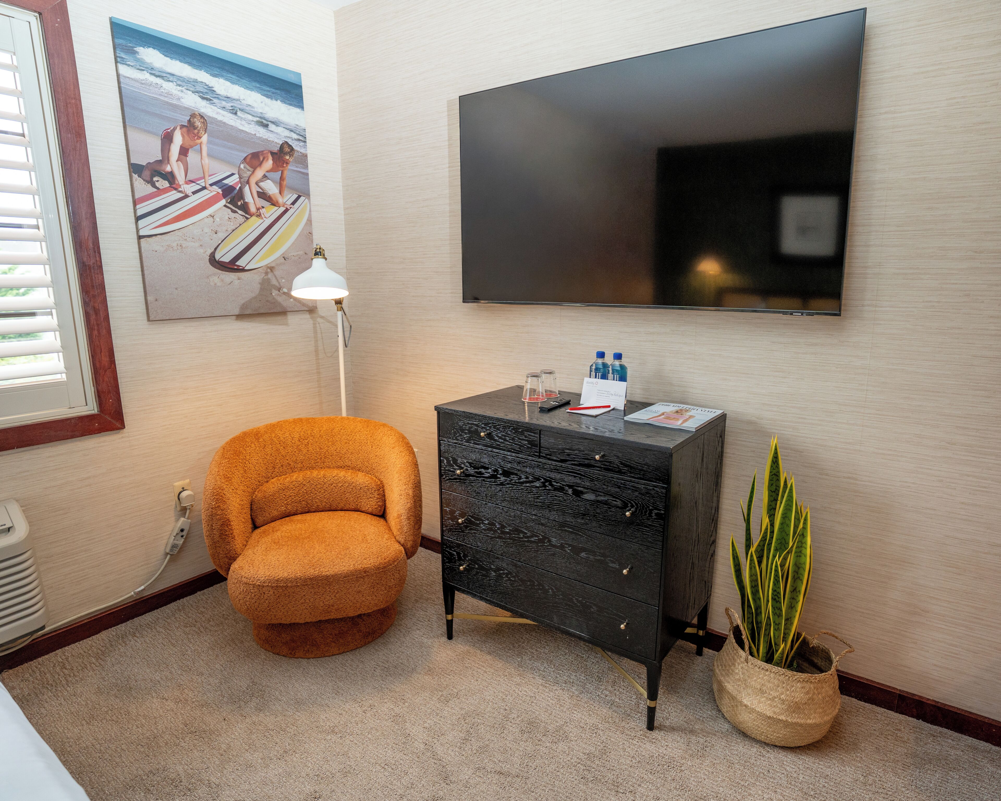 A room with a sofa, a TV, a desk with a lamp, a plant, and a painting.