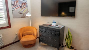 A room with a sofa, a TV, a desk with a lamp, a plant, and a painting.