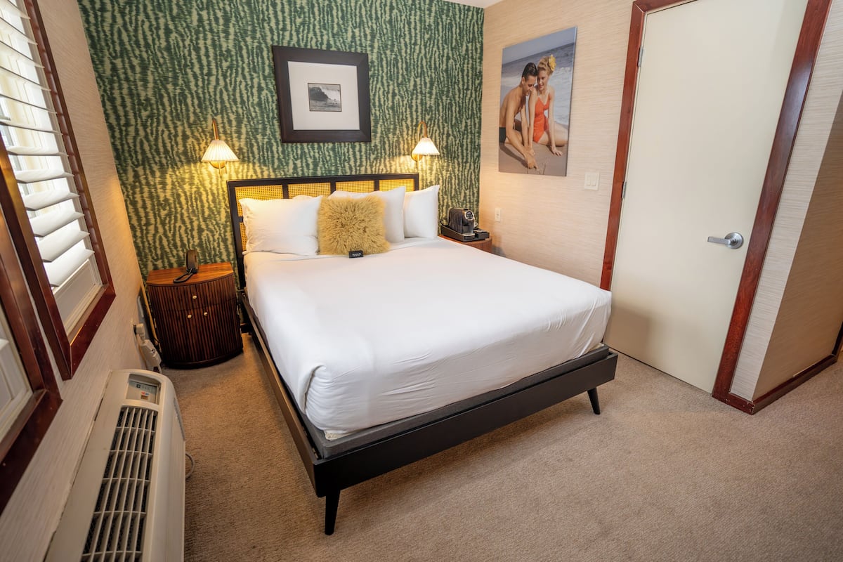 A hotel room with a bed, two bedside lamps, a wall-mounted picture, and a door.