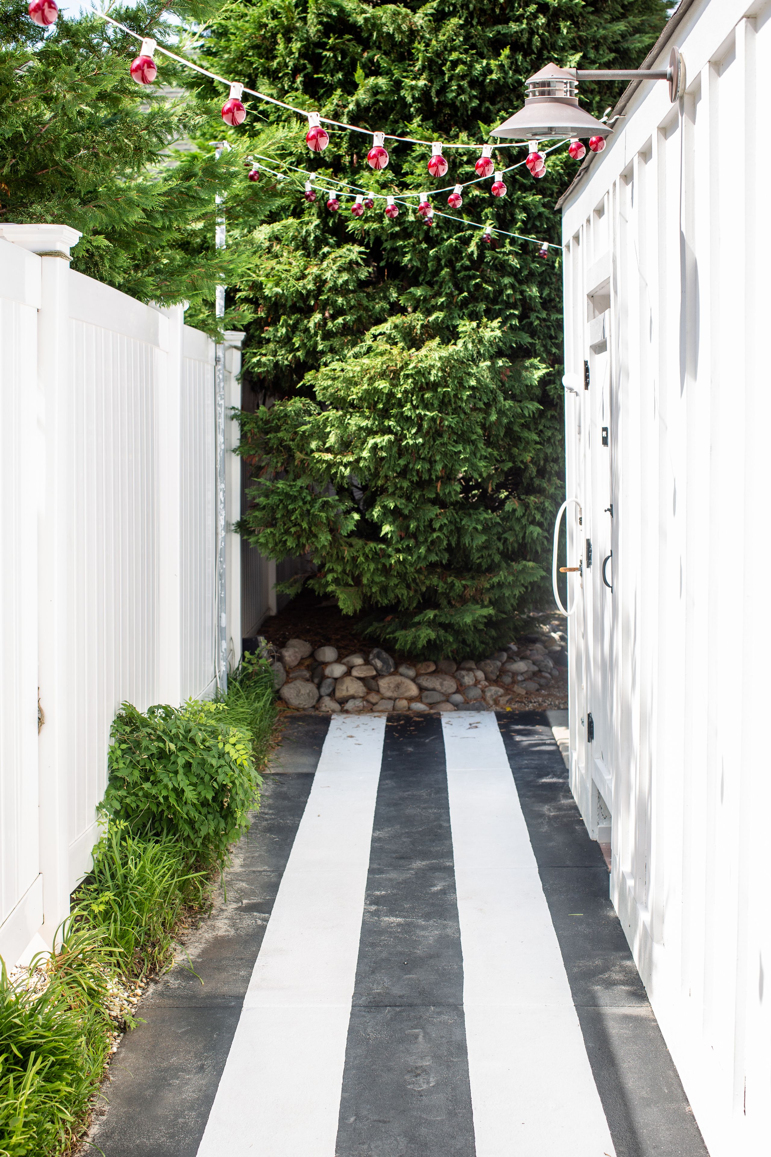 A narrow pathway flanked by white fences and a stone wall, leading to a building with a white exterior.