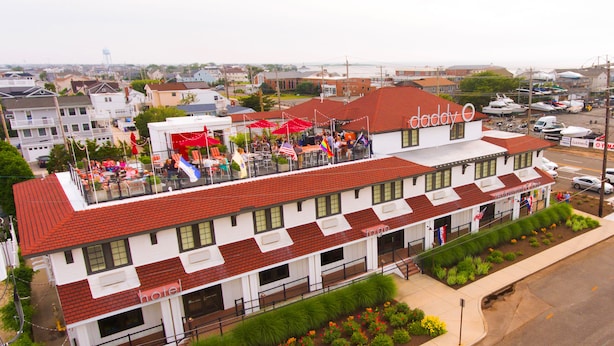 A multi-story hotel with a red roof and white facade, featuring outdoor seating areas and a landscaped garden. - Daddy O Hotel (Beach Haven)
