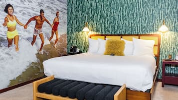Un dormitorio con una cama grande, cabecera con luces, un mural en la pared y un banco de madera.