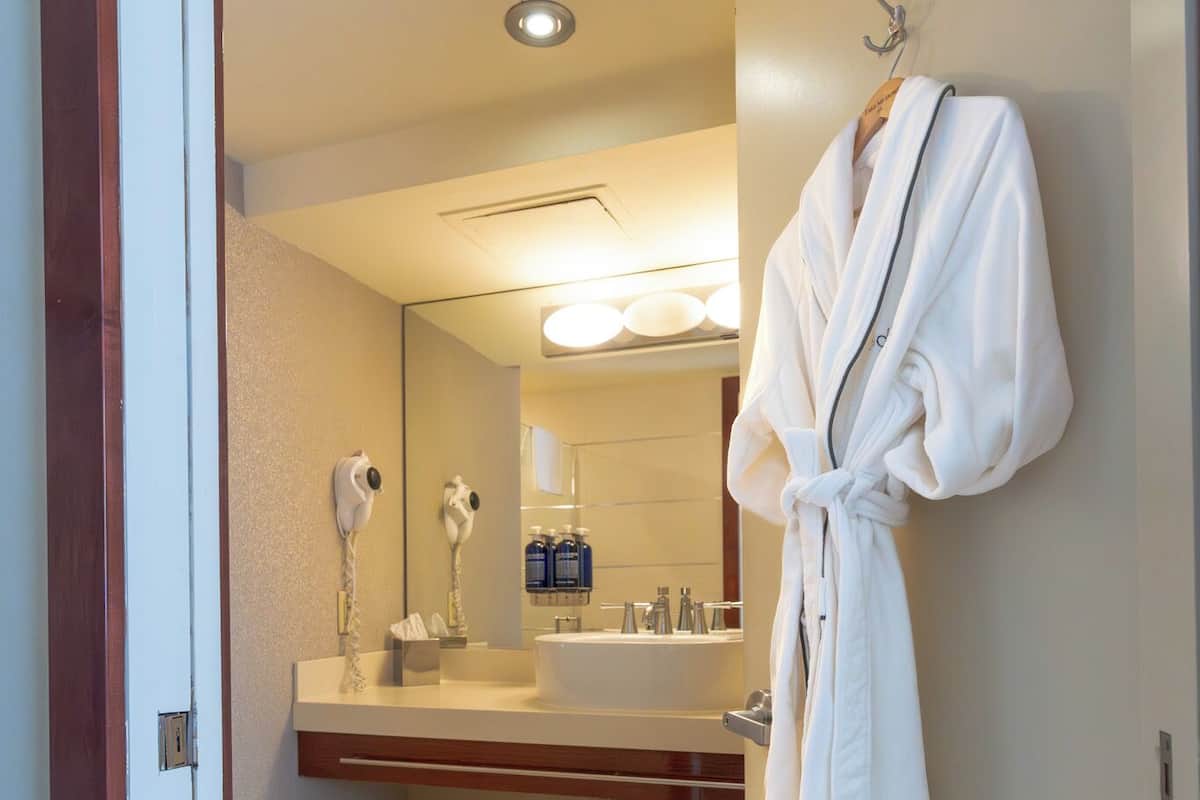 A hotel bathroom with a white robe hanging on the wall, a sink, and a trash bin.
