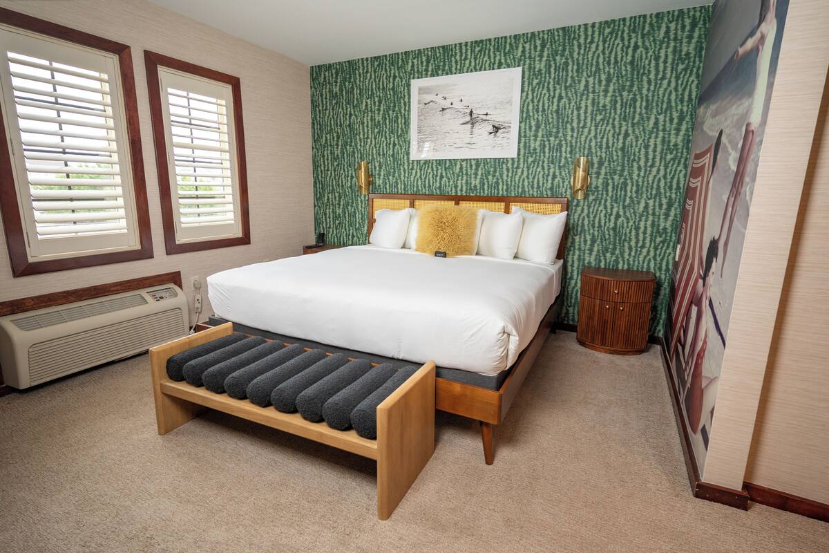 A bedroom with a bed, a bench, a heater, and a wall with a picture.