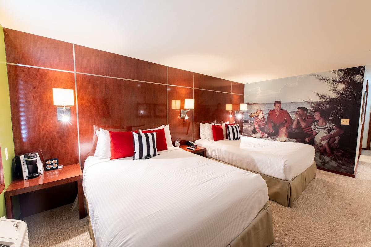A hotel room with two beds, a nightstand with a coffee maker, and a large painting on the wall.