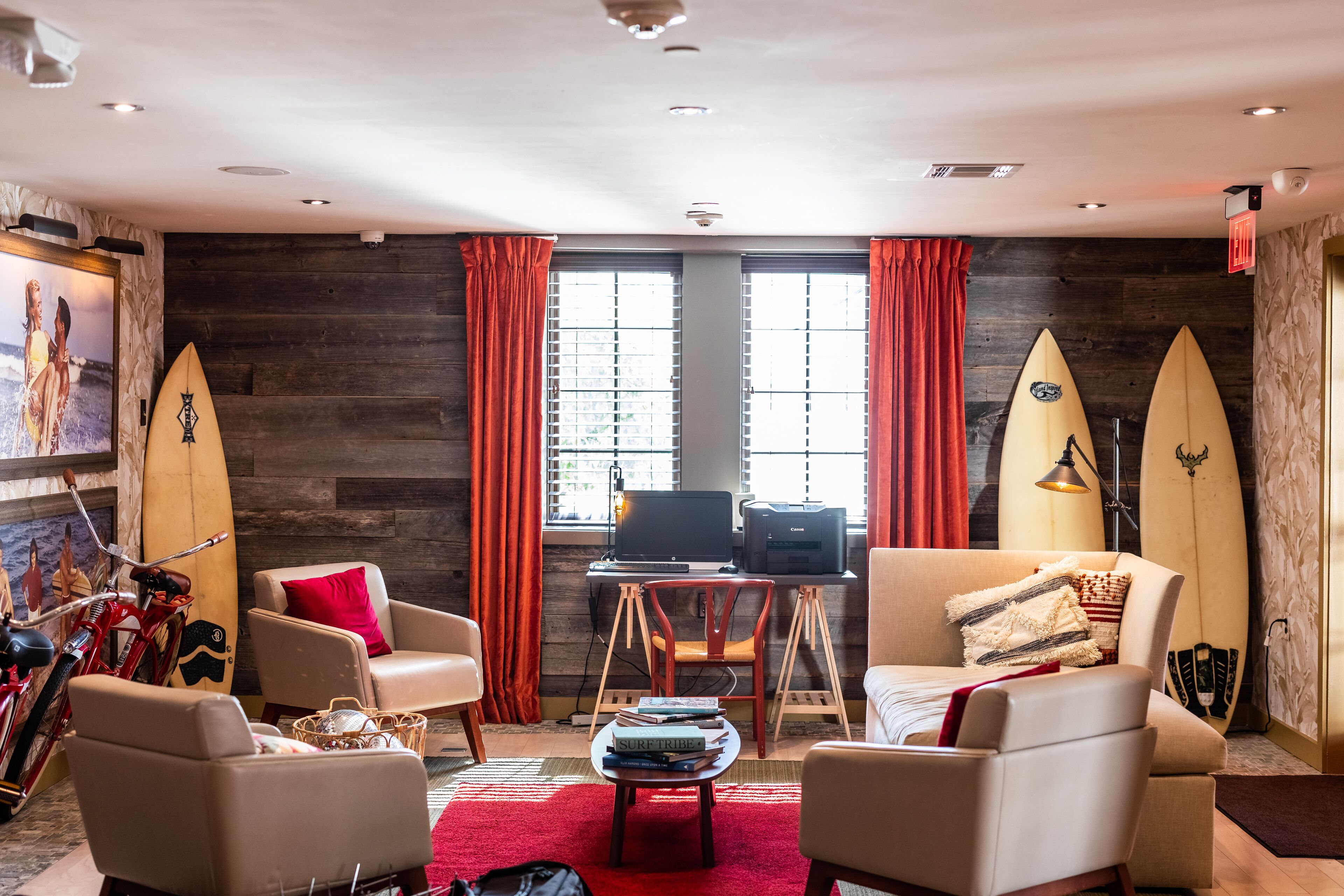 A room with two leather armchairs, a small table with books, a desk with a computer, and two surfboards leaning against the wall.