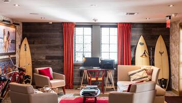 A room with two leather armchairs, a small table with books, a desk with a computer, and two surfboards leaning against the wall.