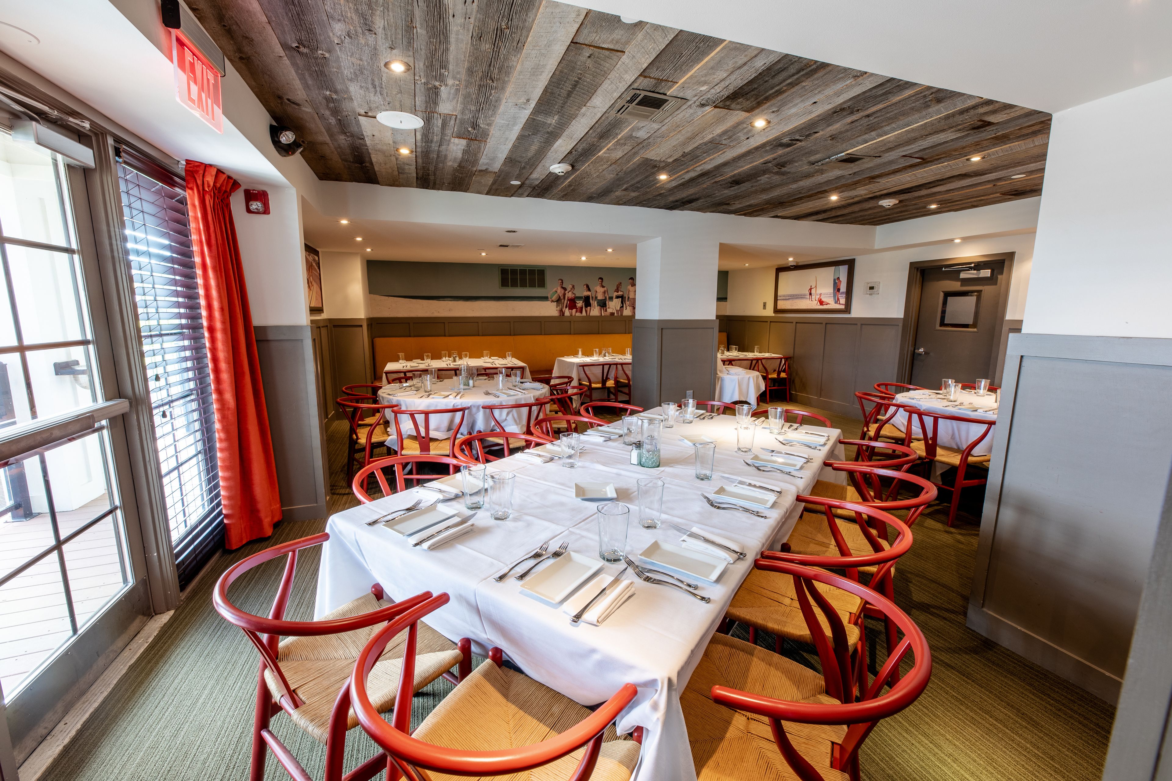 A restaurant with a long table set for dining, red chairs, and a wooden ceiling.