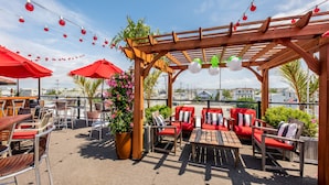 An outdoor patio area with wooden tables and chairs, red umbrellas, and string lights. - Daddy O Hotel (Beach Haven)