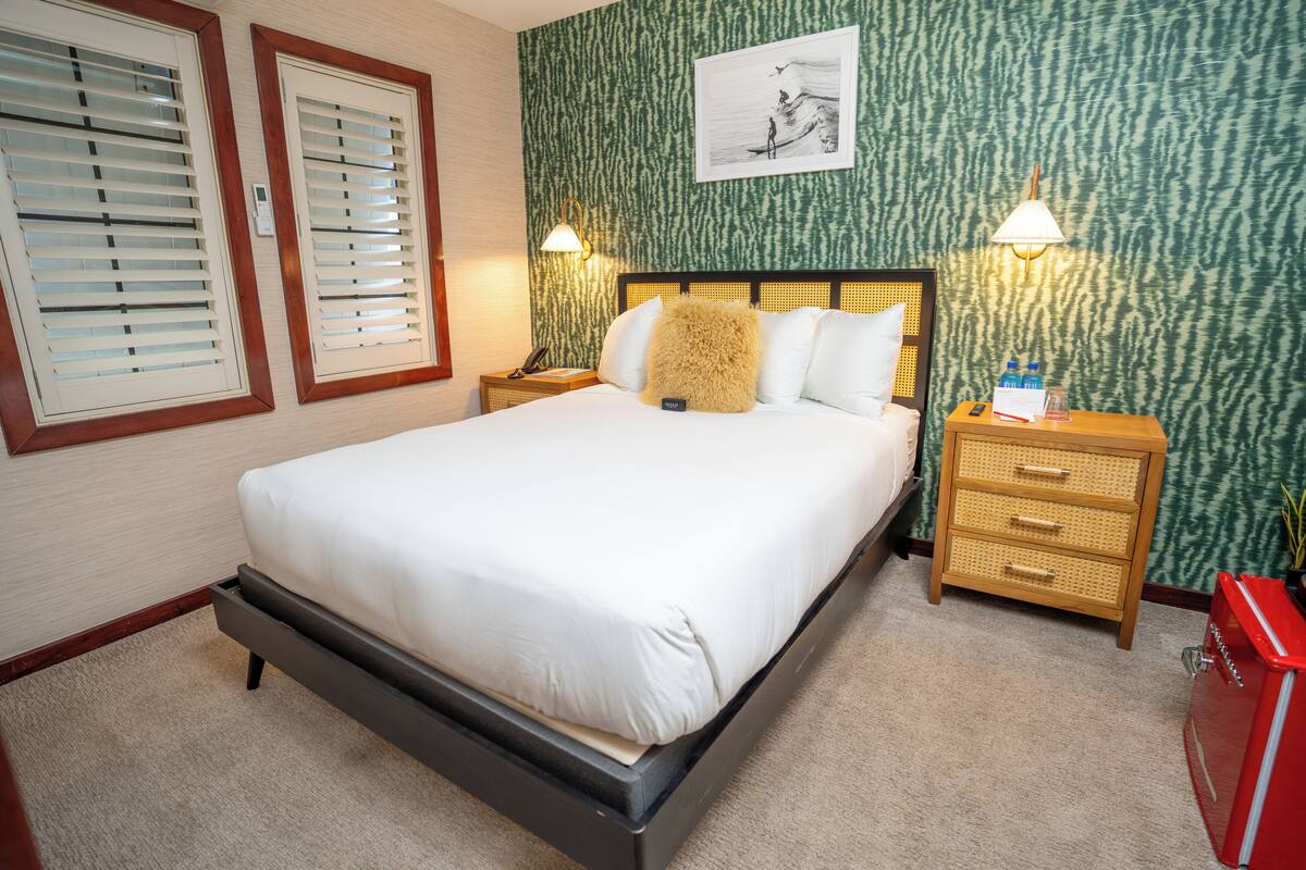 A bedroom with a bed, two bedside tables, a nightstand, a lamp, a wall-mounted picture, and a red cabinet.