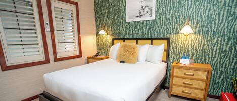 A bedroom with a bed, two bedside tables, a nightstand, a lamp, a wall-mounted picture, and a red cabinet.