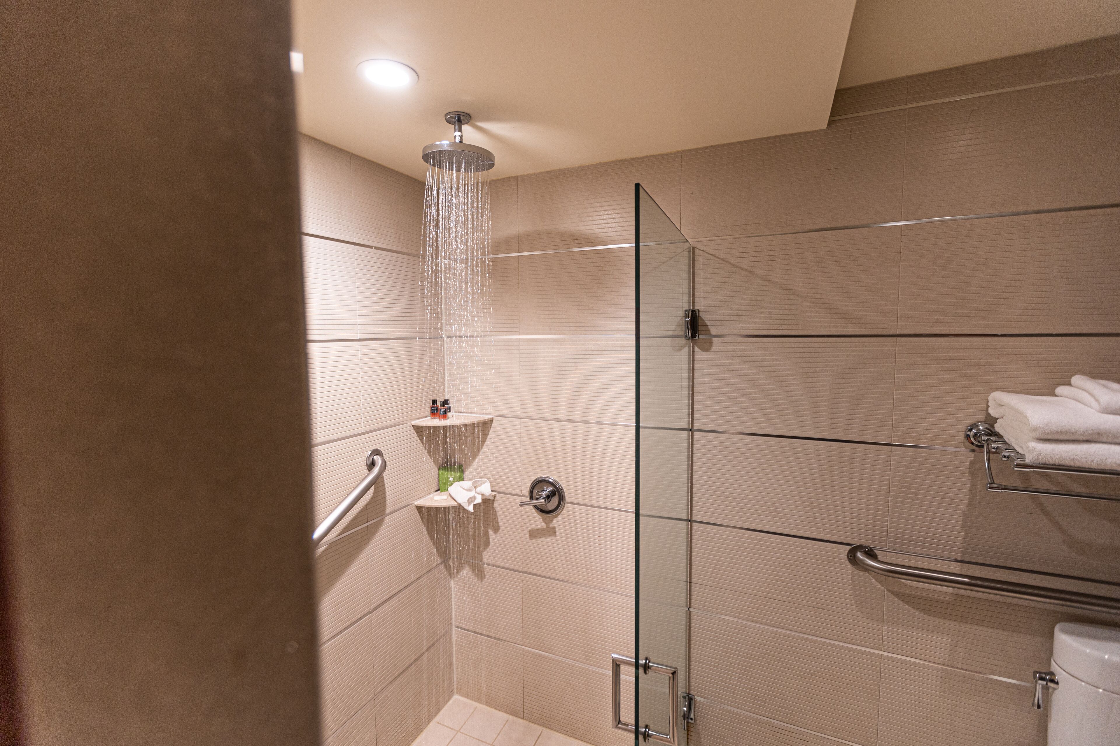 A modern shower with a glass door, a handrail, and a towel rack with folded towels.
