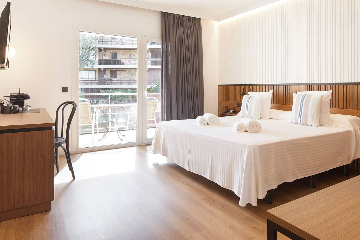 A hotel room with a bed, a desk, a chair, and a view of the outside balcony.