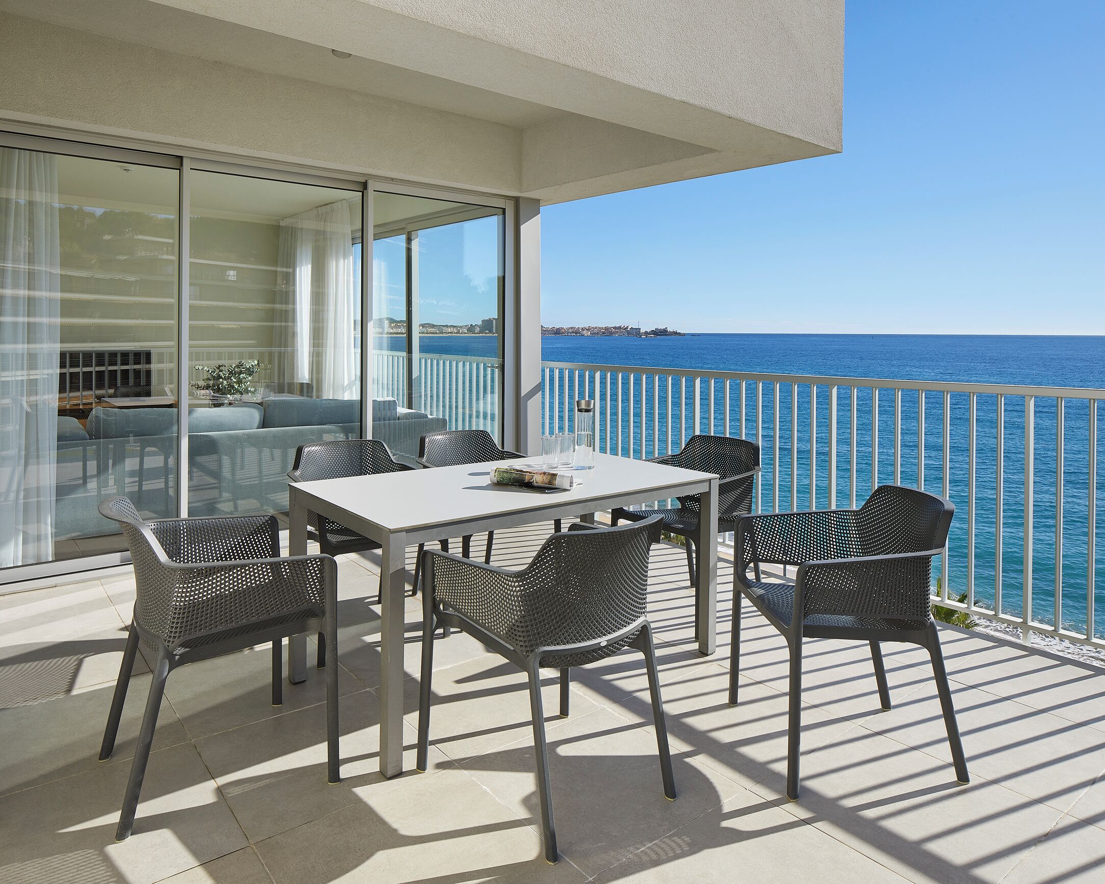 A balcony with a white table and chairs, overlooking a body of water.