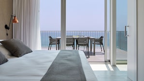 A hotel room with a bed, a table with chairs, and a view of the sea through large glass doors.