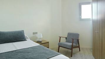 Un dormitorio con cama, una silla, una mesita de noche con lámpara y un armario.