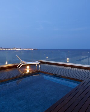 A pool area with a lounge chair and a small table, surrounded by a wooden deck.